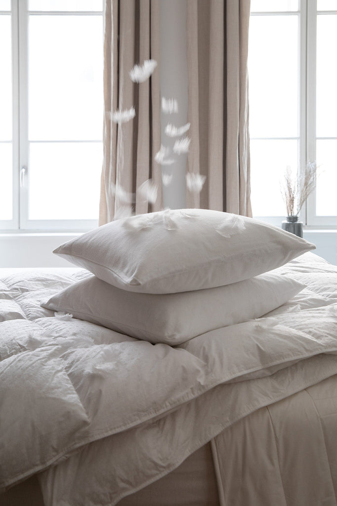 white bedding with feathers floating on top of the pillows